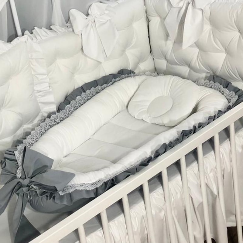 Baby Nest Volle, vedere de ansamblu Baby Nest Volle alb cu volan gri tivit cu dantelă, fundă gri și pernuță mică, într-un pătuț