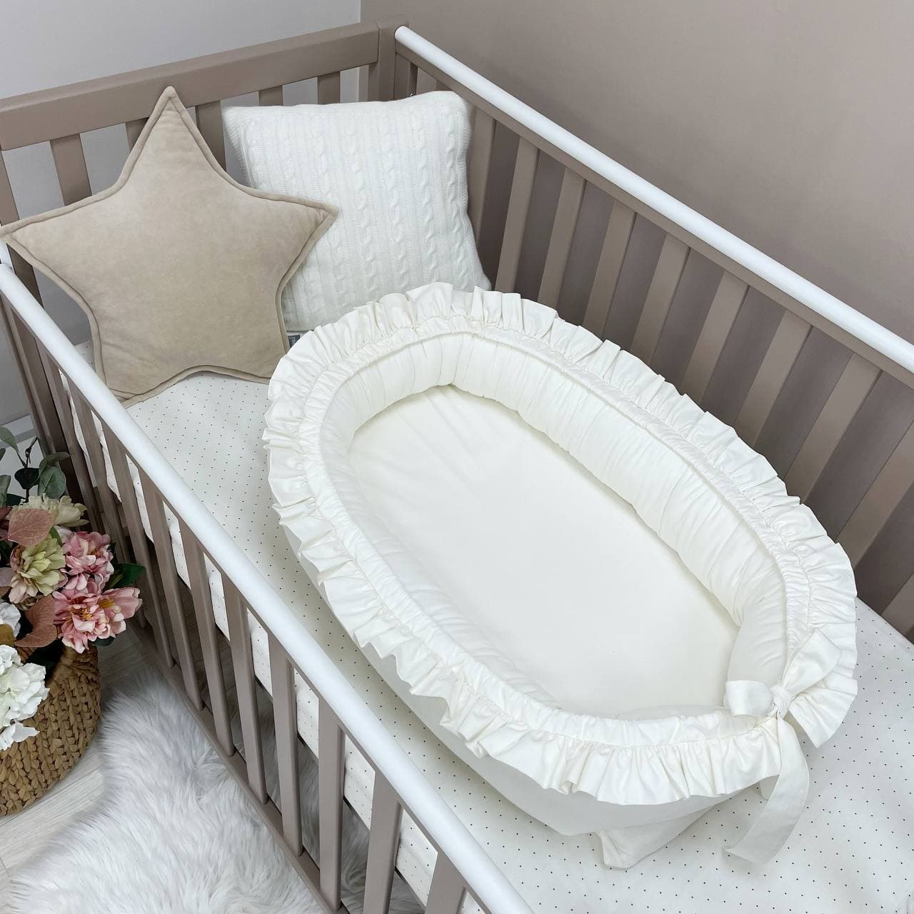Baby nest Universal, vedere de ansamblu Baby nest Universal fotografiat în varianta albă cu volănașe și fundă, într-un pătuț