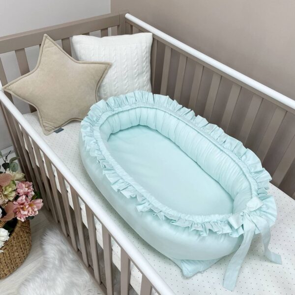 Baby nest mentă cu volănașe, cu fundă la picioare, fotografiat într-un pătuț