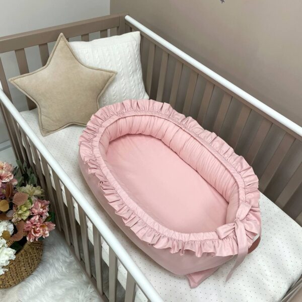 Baby nest roz cu volănașe și fundă la picioare, fotografiat într-un pătuț