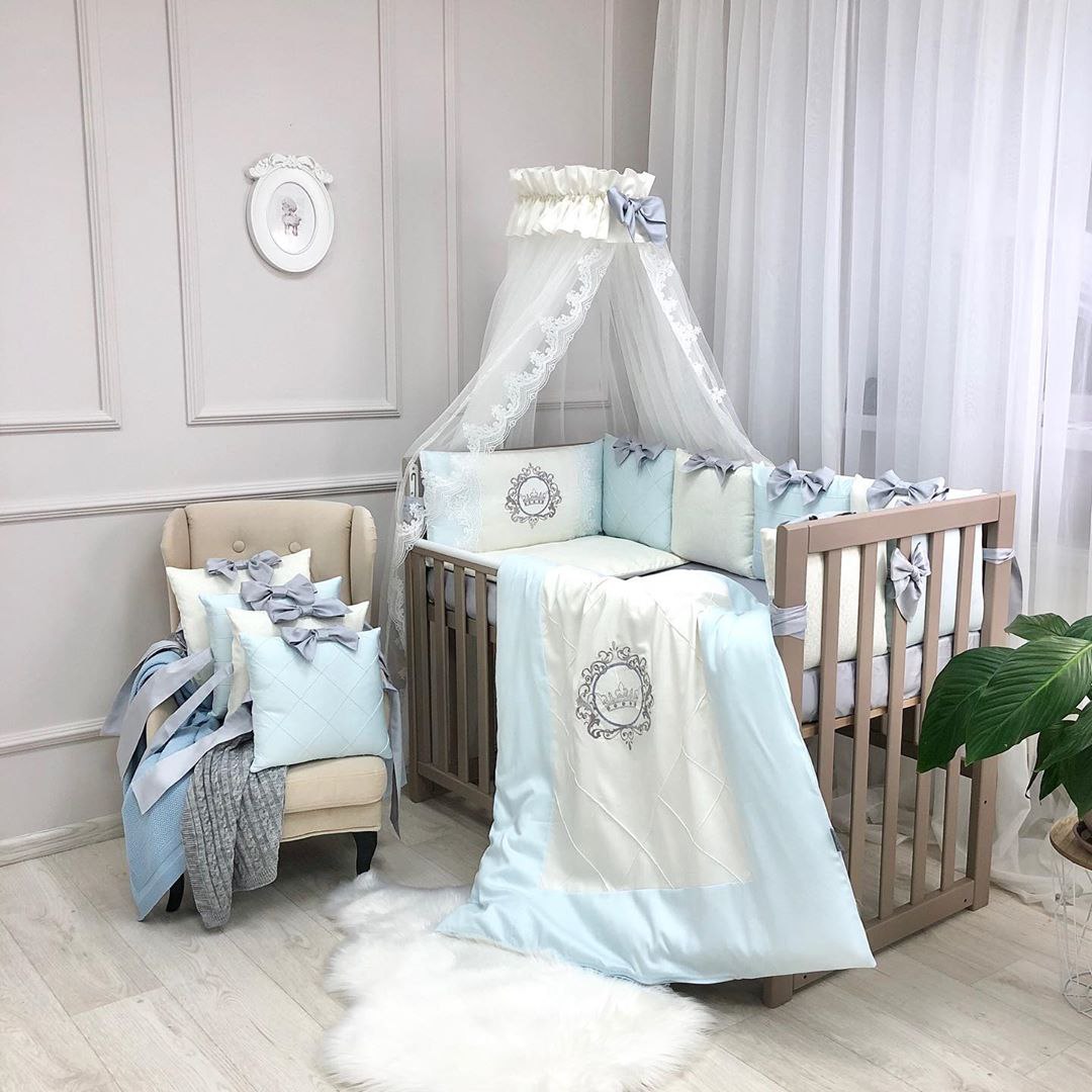 Elegance blue, pătuț îmbrăcat Pătuț din lemn cu lenjeria Elegance blue și baldachin din tul, lângă un fotoliu cu pernuțe bleu