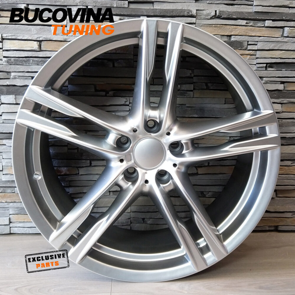 Jantă R20 stil M Hyper Silver, vedere din față Jantă R20 5×120 Hyper Silver în stil M, cu cinci spițe duble, sprijinită de un perete de piatră