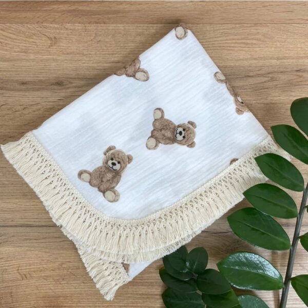 Păturică cu ursuleți Teddy și franjuri crem, împăturită pe o masă din lemn