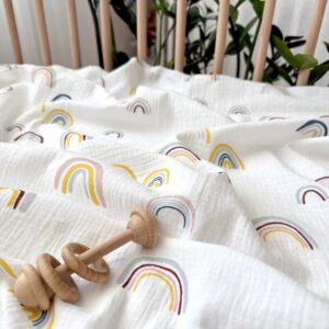 Detaliu de curcubee în galben, roz, gri și bleumarin pe muselină albă, lângă o jucărie din lemn