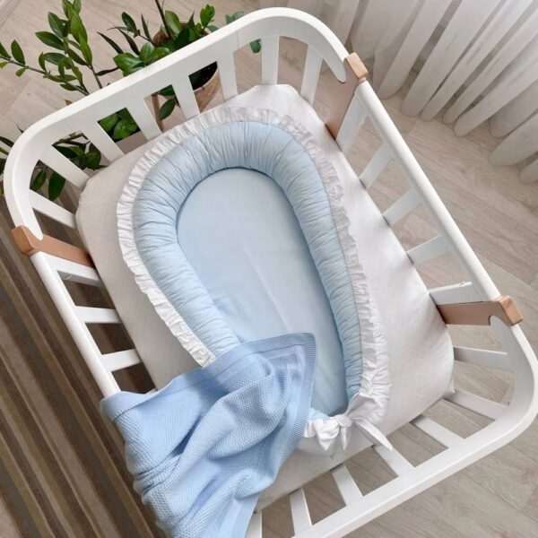 Baby nest cu două fețe alb-albastru, fața bleu cu volan alb și fundă albă, vedere de sus
