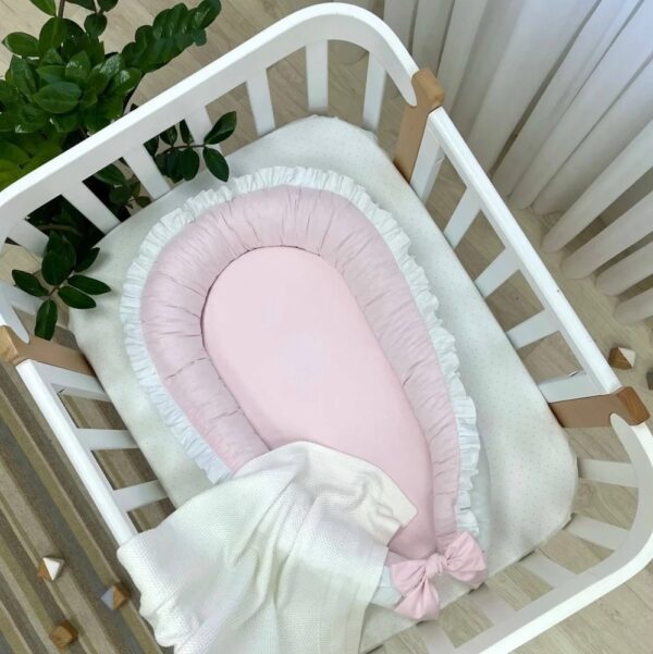 Baby nest cu două fețe alb-roz, fața roz pal cu volan alb și fundă roz, vedere de sus
