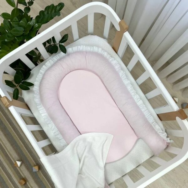 Fața roz pal a baby nest-ului alb-roz, cu margini capitonate și volan alb