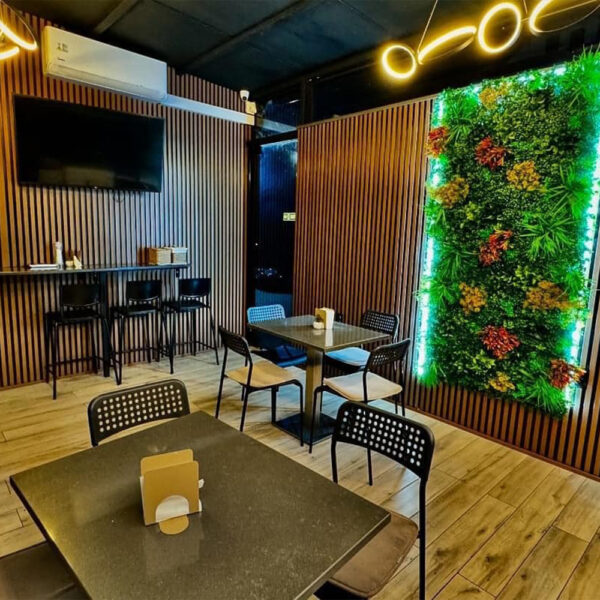 Cafenea cu pereți placați cu riflaj de lemn și perete cu vegetație decorativă iluminat