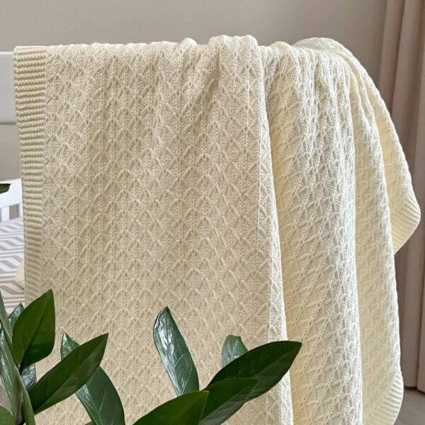 Păturica Confort milky căzând în falduri, cu modelul geometric și bordura cu nervuri, lângă o plantă