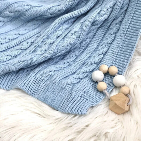 Colțul păturicii albastre cu torsadele și bordura tricotată, pe o blăniță, lângă jucării din lemn