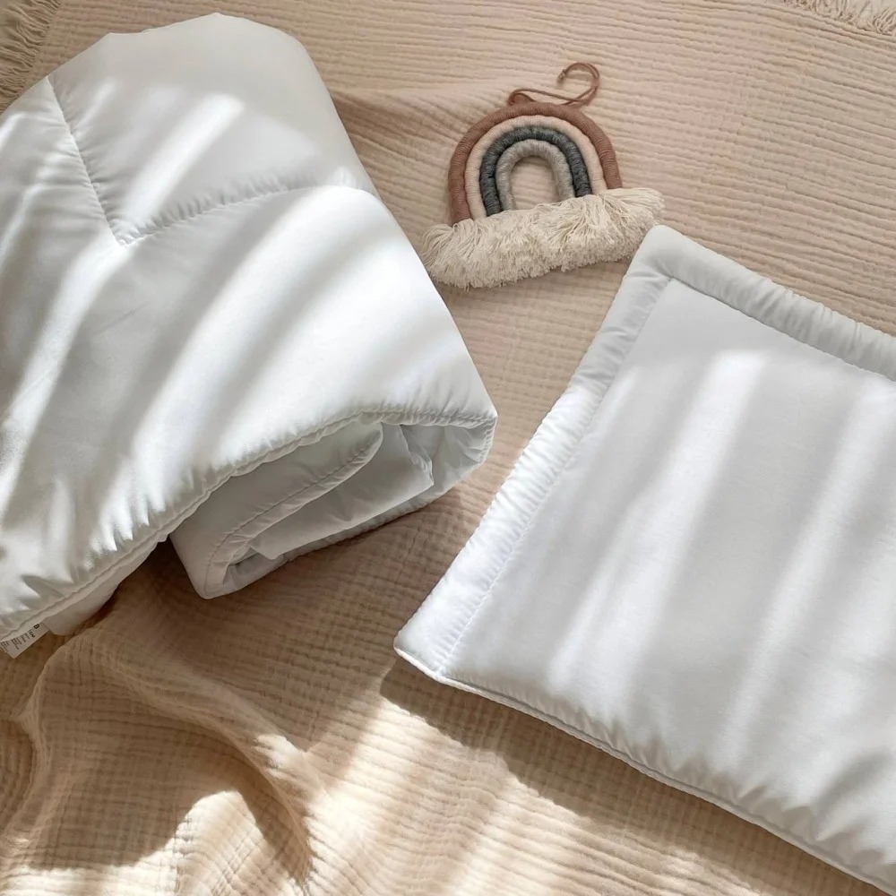 Set pernă și pilotă cu puf artificial de lebădă Pilotă albă împăturită și pernă plată din microfibră, așezate pe o pătură bej de muselină