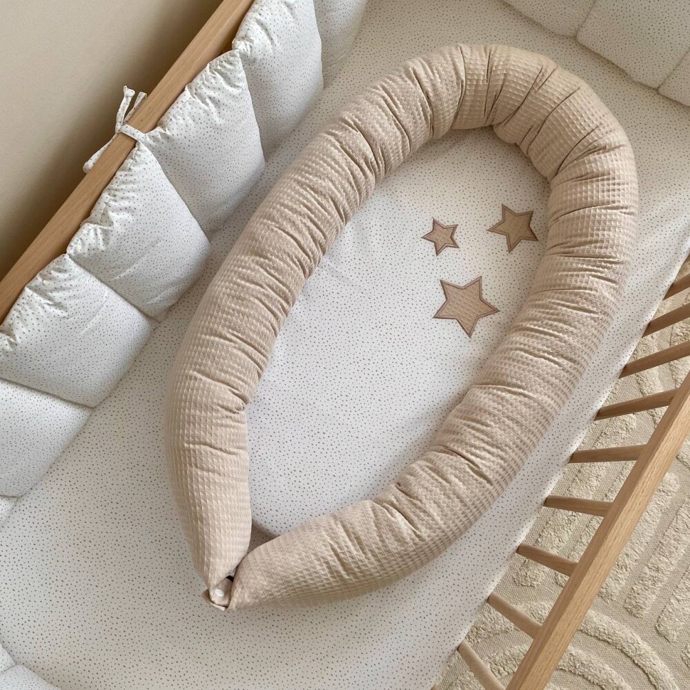 Baby Nest Stars vafe bej, vedere de sus Baby Nest Stars vafe bej cu steluțe cusute pe saltea, într-un pătuț, vedere de sus