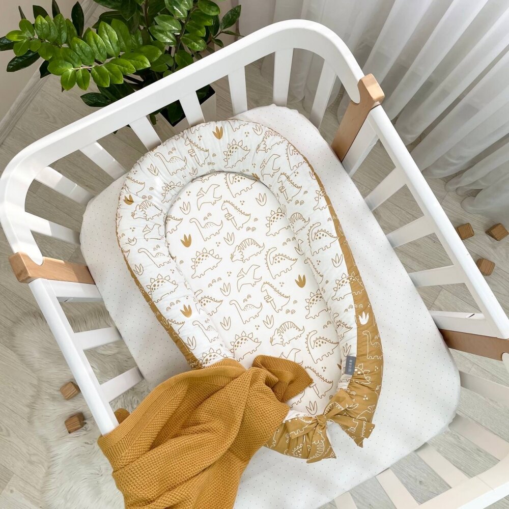Baby nest Dino muștar Baby nest Dino muștar cu dinozauri conturați în muștar pe fond alb și fundă muștar, în pătuț