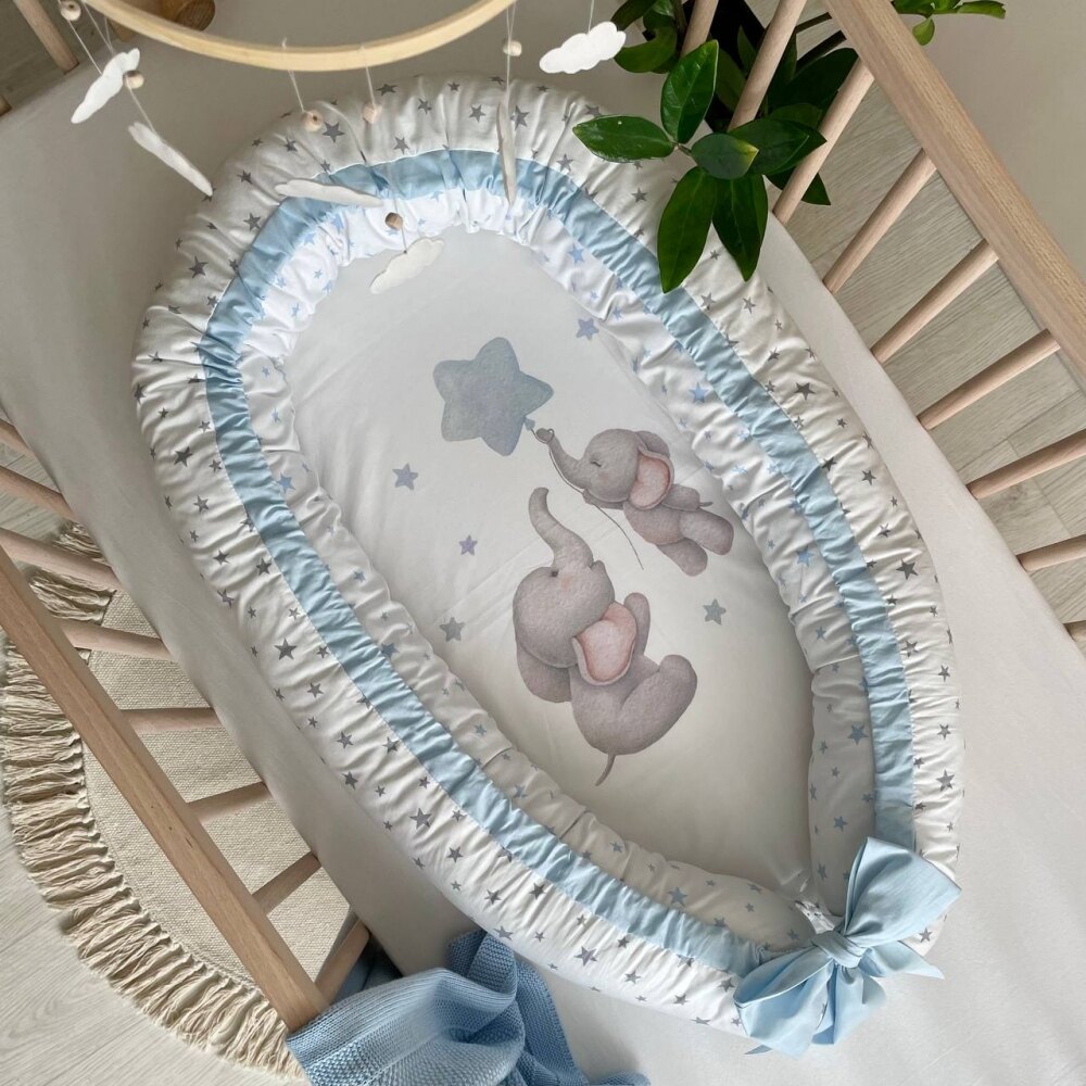 Baby Nest Familia elefănțel, vedere de sus Baby Nest Familia elefănțel cu elefănței pe saltea, volan bleu și fundă bleu, vedere de sus