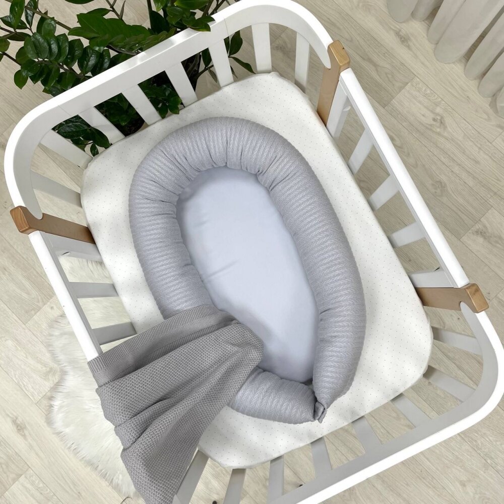Baby Nest Velvet gri, vedere de sus Baby Nest Velvet gri cu margine din tricot împletit și saltea netedă, într-un pătuț alb, vedere de sus