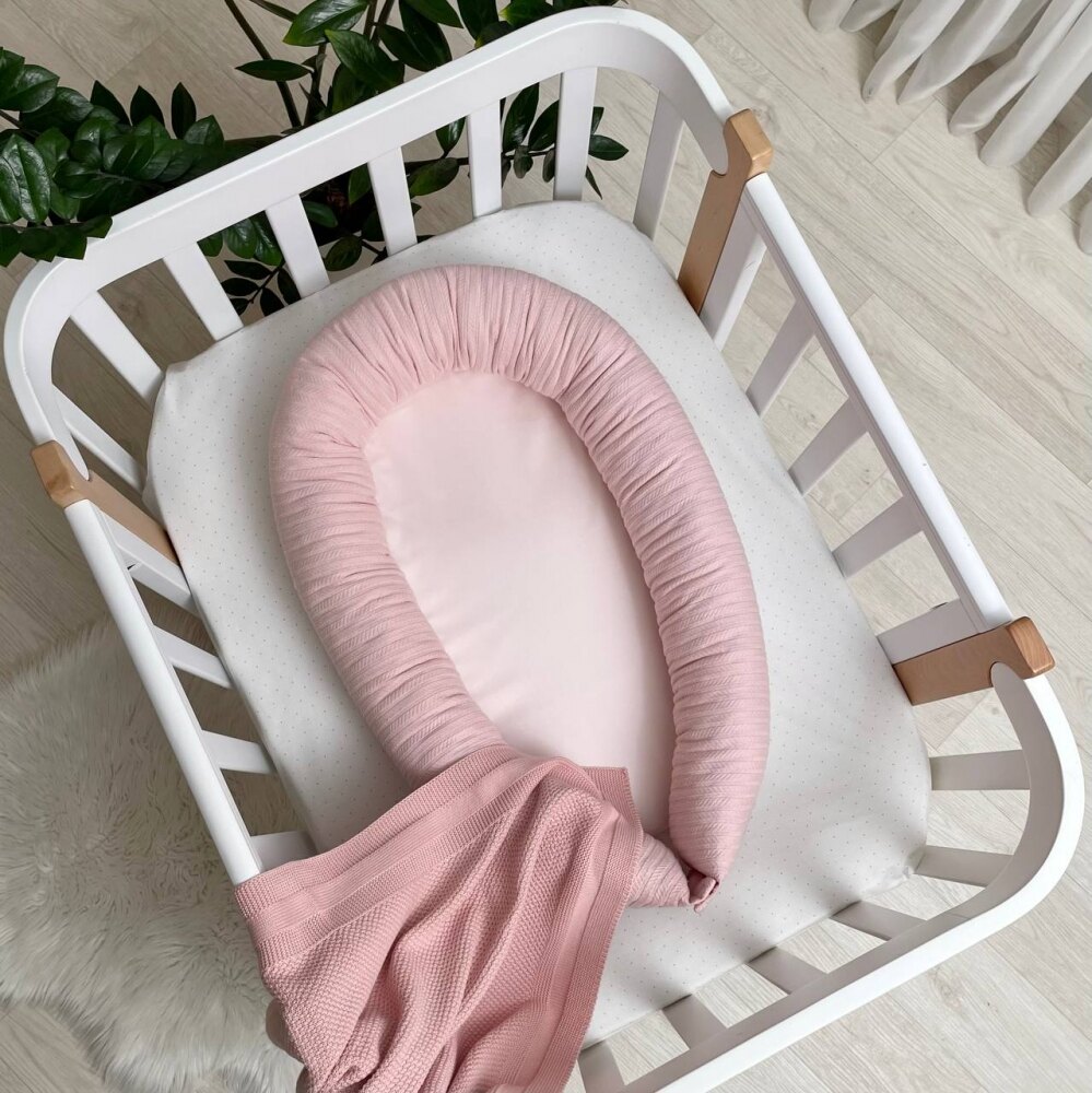 Baby Nest Velvet roz, vedere de sus Baby Nest Velvet roz cu margine din tricot împletit, într-un pătuț alb, vedere de sus