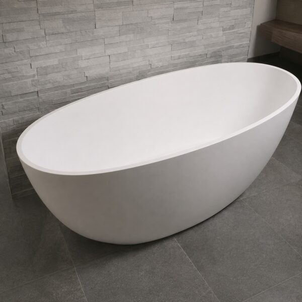 Cadă freestanding ovală 2130230 din compozit alb mat, într-o baie cu perete din piatră gri