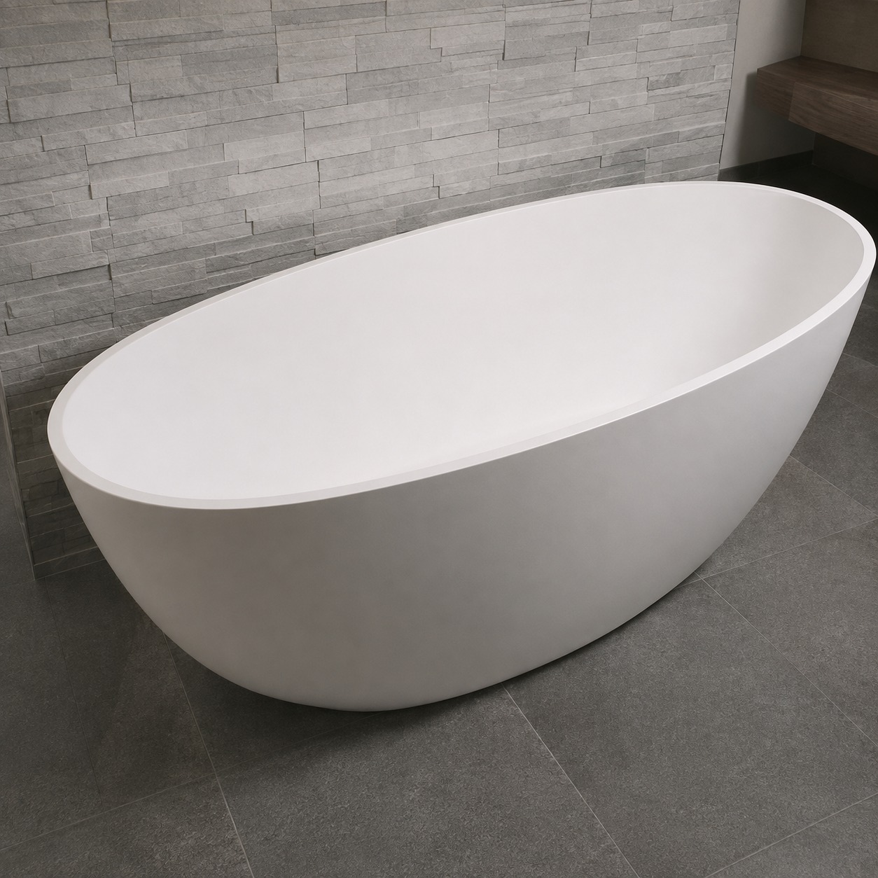 Cadă freestanding 2130230 din compozit alb mat Cadă freestanding ovală 2130230 din compozit alb mat, într-o baie cu perete din piatră gri