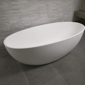 Cadă freestanding 2130250 din compozit alb mat, formă ovală, într-o baie cu perete din piatră gri