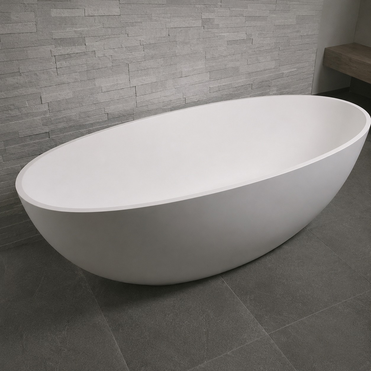 Cadă freestanding 2130250 din compozit alb mat Cadă freestanding 2130250 din compozit alb mat, formă ovală, într-o baie cu perete din piatră gri