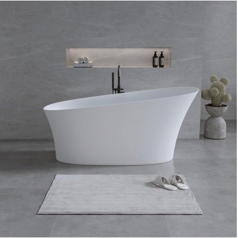 Cadă din compozit 2130320 – vedere frontală Cadă freestanding 2130320 din compozit alb mat, cu un capăt înălțat, într-o baie cu pereți gri