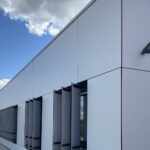 Fațada lungă a unei clădiri universitare din plăci albe Fundermax 0085 White, cu rosturi negre și parasolare verticale albe