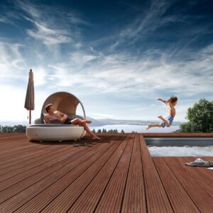 Deck din Massaranduba maro-roșcat lângă o piscină, cu un bărbat întins sub copertina unui pat de soare și un copil în salt spre apă