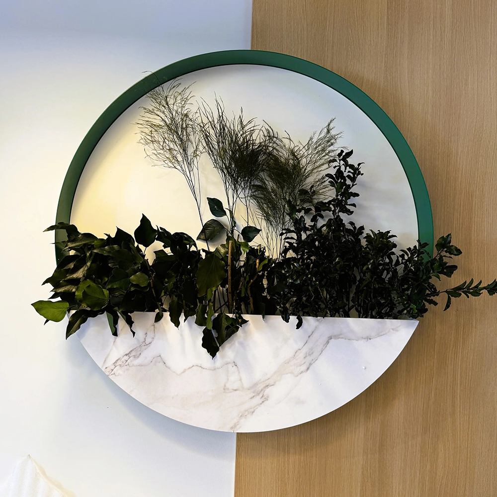 Decor rotund cu ruscus, ferigă și eucalipt stabilizate Decor rotund de 65 cm cu ramă verde închis, fundal alb și plante stabilizate pe bază cu aspect de marmură albă