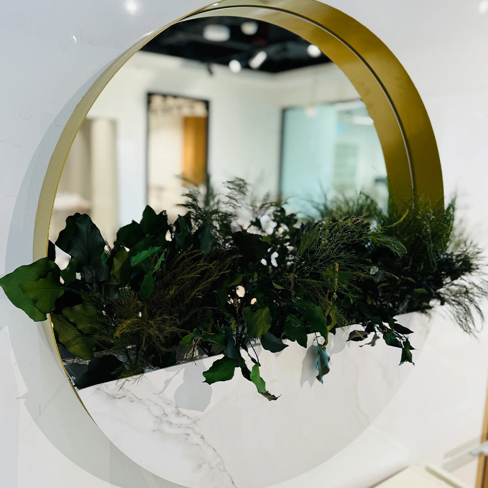 Decor rotund cu oglindă, ramă aurie și plante stabilizate Decor rotund de 65 cm cu ramă aurie adâncă, oglindă centrală și plante stabilizate verde închis pe bază albă marmorată