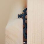 Distanțier Fugo negru montat, în prim-plan: profilul lui dințat, văzut din capăt, prins între șipca verticală și scândurile de lemn deschis