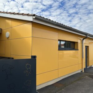Clădire cu parterul placat cu panouri lucioase galben-șofran în decorul Fundermax 0736 Saffron, sub o streașină cu țiglă