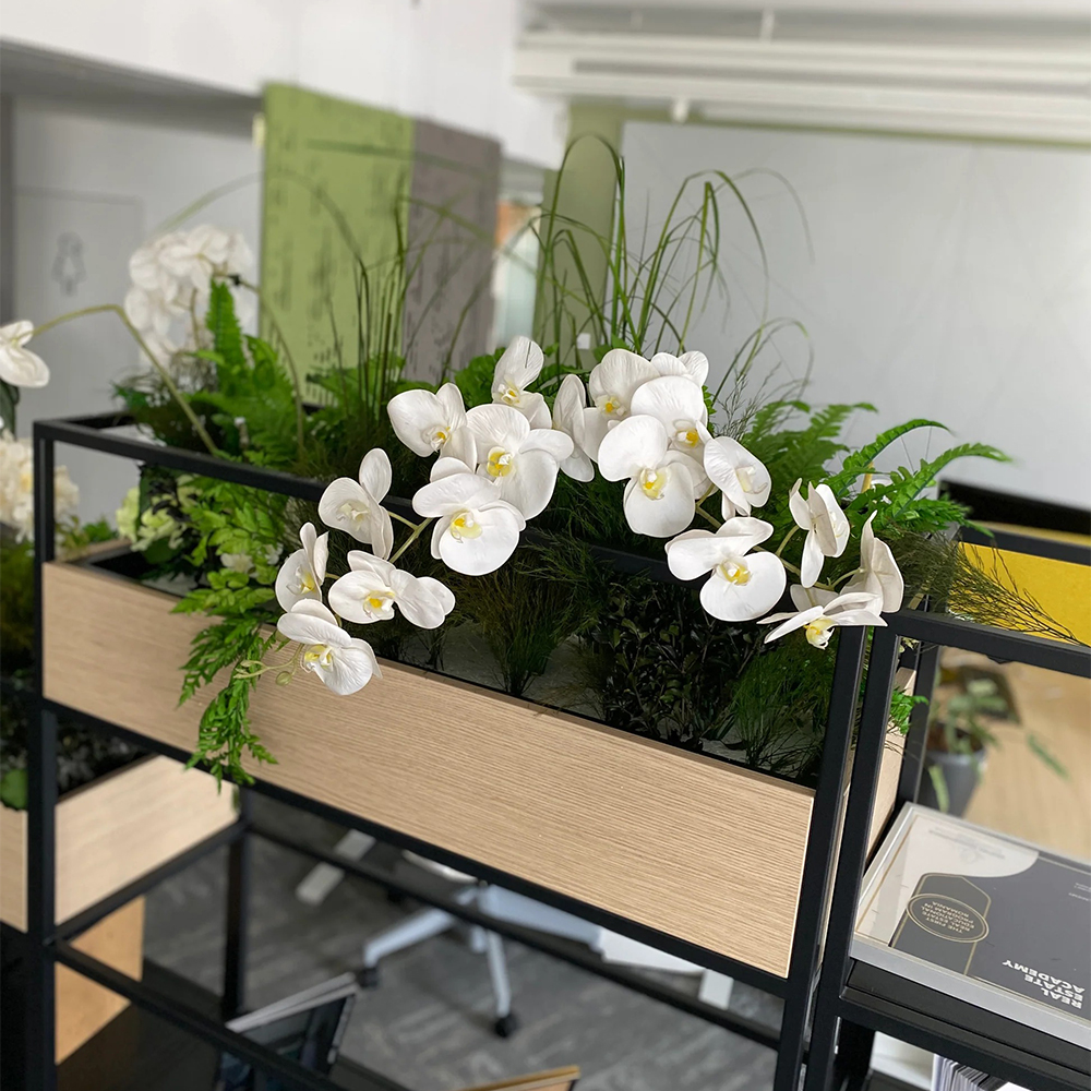 Jardinieră cu plante artificiale și orhidee albe Jardinieră cu aspect de lemn deschis în raft metalic negru, cu orhidee albe, ferigi și ierburi artificiale, într-un birou