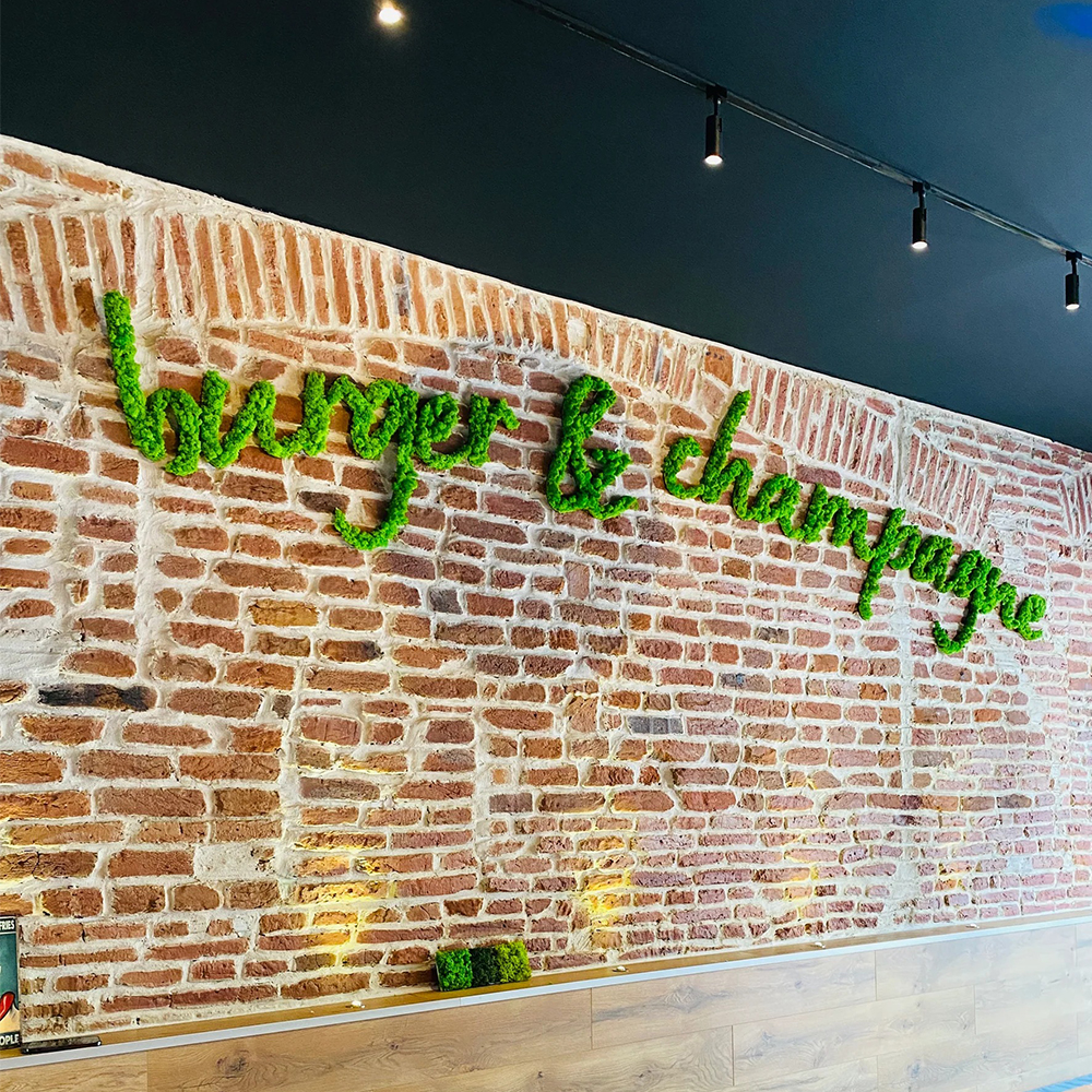 Litere volumetrice din licheni verzi pe cărămidă Inscripție cursivă din litere volumetrice cu licheni verzi pe un perete de cărămidă aparentă, într-un restaurant