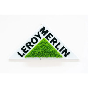 Logo din licheni verzi și litere negre pe o placă albă triunghiulară, montată pe perete