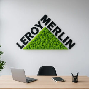 Logo din licheni stabilizați verzi cu litere negre în relief, pe peretele unui birou, deasupra unei mese de lucru