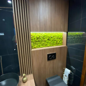 Baie cu faianță neagră și mobilier din lemn, cu panou din licheni verde crud într-o nișă luminată