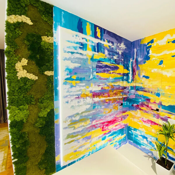 Panou vertical din licheni și mușchi lângă un perete de colț pictat abstract în galben, albastru și violet