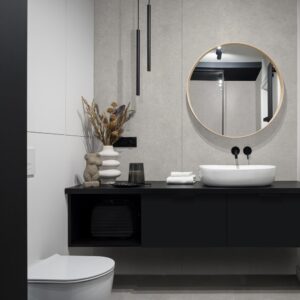 Baie cu mobilier suspendat negru, lavoar oval alb și oglindă rotundă cu ramă din lemn, pe un perete Rocko R159 Soulstone