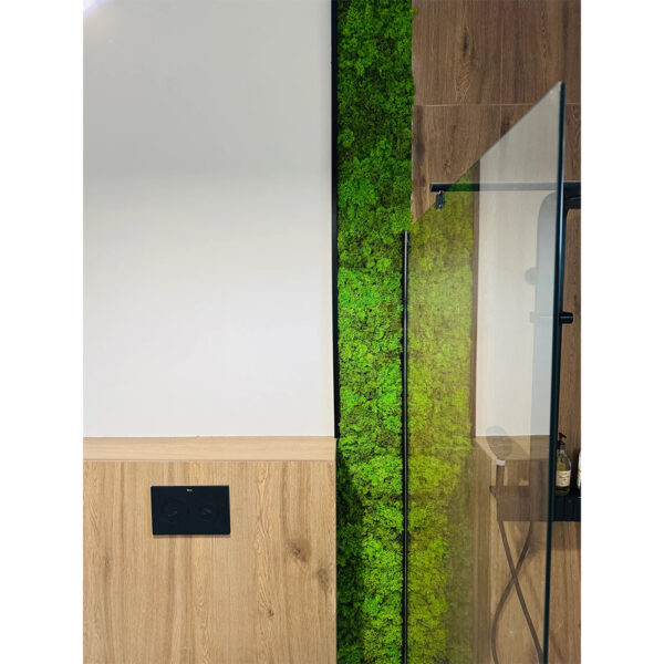 Panou vertical îngust din licheni verde viu între un perete alb și paravanul de sticlă al unui duș