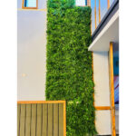 Coloană înaltă din plante artificiale verzi pe peretele unui spațiu cu înălțime dublă, lângă o ușă