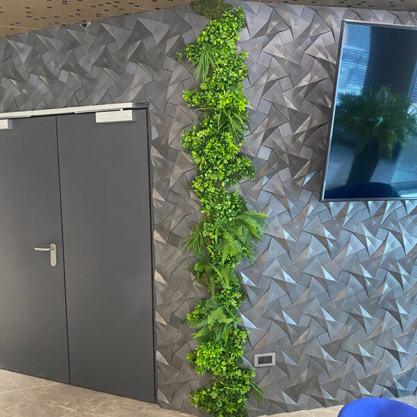 Coloană verticală de plante artificiale pe un perete cu panouri 3D gri, lângă o ușă și un televizor