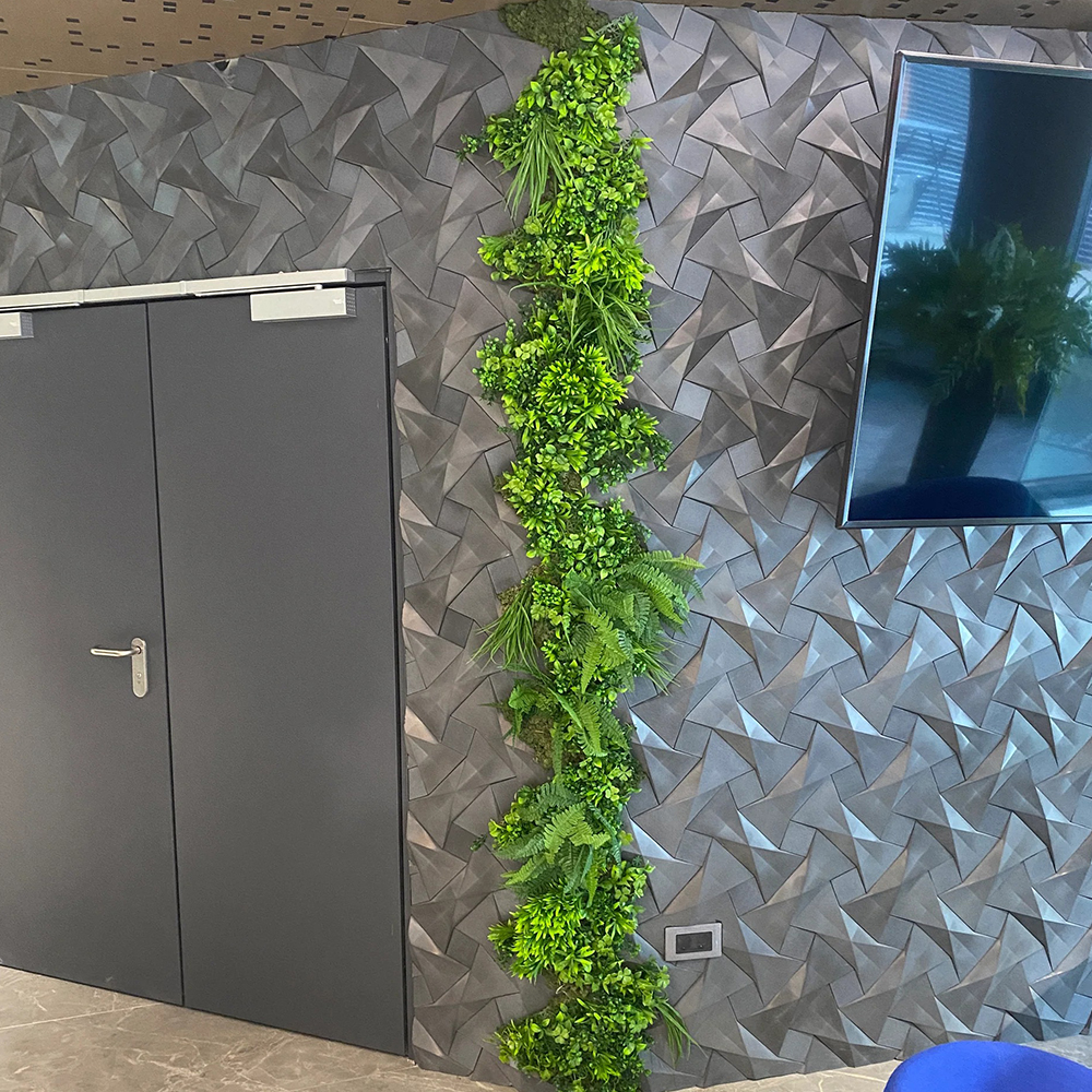 Coloană verde artificială lângă o ușă Coloană verticală de plante artificiale pe un perete cu panouri 3D gri, lângă o ușă și un televizor