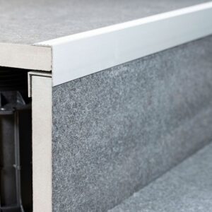 Profil de contur Relo RA din aluminiu montat pe marginea unei terase din dale gri, cu structura vizibilă dedesubt