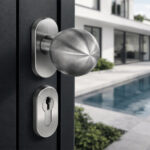 Buton sferic din inox montat pe o poartă neagră, cu rozeta pentru yală sub el, lângă o piscină