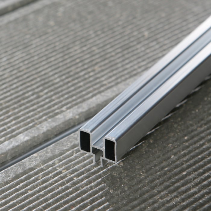 Șina de aluminiu UPM ProFi ALU RAIL așezată în rostul dintre două plăci WPC gri striate, văzută dinspre capăt Șina de aluminiu UPM ProFi ALU RAIL așezată în rostul dintre două plăci WPC gri striate, văzută dinspre capăt