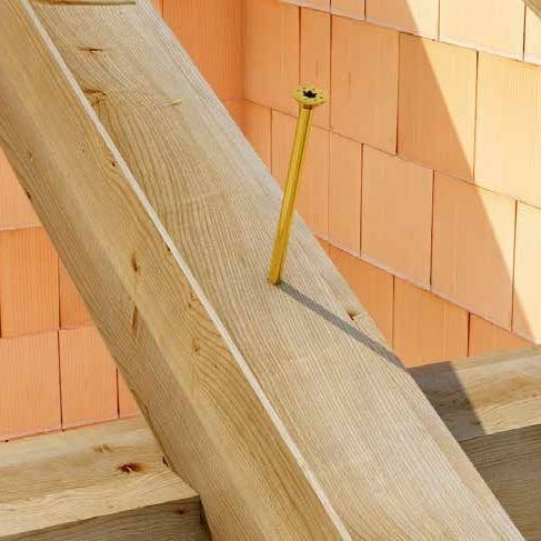 Șurub de dulgherie Holz Technic SCH-H zincat galben, înșurubat pe jumătate într-o grindă înclinată, lângă un zid de cărămidă