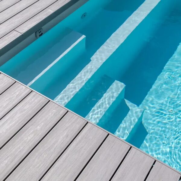 Margine de piscină cu trepte, încadrată de plăci UPM ProFi Piazza Silver Teak gri deschis, cu apă turcoaz în lumina soarelui